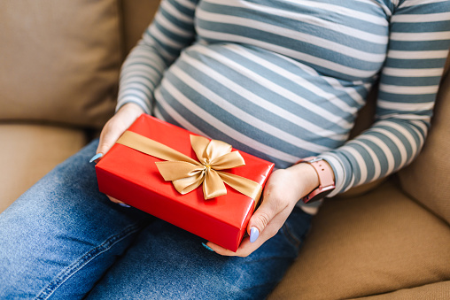 Young pregnant woman holding a gift with a ribbon