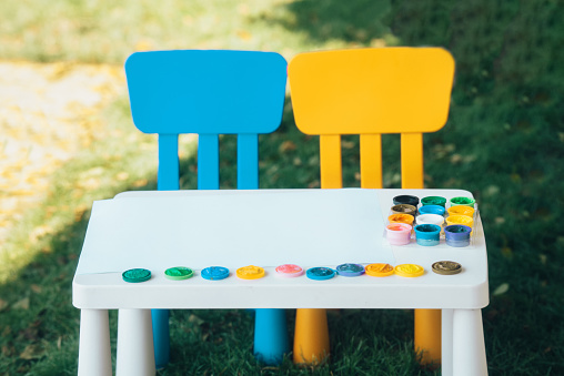 children's table and colored chairs with gouache paints outdoors. Children's background is bright with copy space. Preschool education