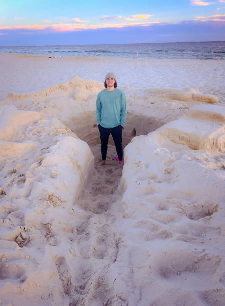 A young man enjoys some fun at the beach, standing in the shape he created in the sand.