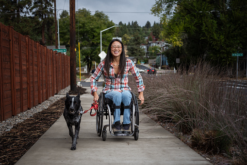 Active Asian woman using a wheelchair while taking her pet dog for a walk