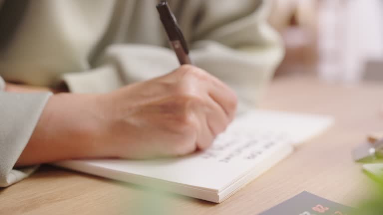 Close up human hand writing New Year Resolutions plan with pen on a plain white blank paper Notebook ,setting Goals in them life for personal improve to success in well being