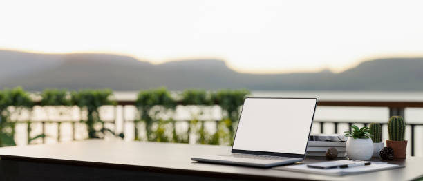 istock Side view of a workspace on a balcony with a white-screen laptop computer mockup on a table. 1839164690