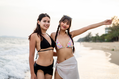 Asian beautiful women friends in bikini walking on the beach together. Attractive young girls traveler feeling happy and relax, running and traveling for holiday vacation trip  in tropical sea island.