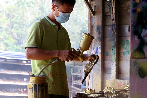 An Asian young man is spraying gold colour on dragon design joss stick sculpture in Factory - Daily Production Activities
