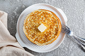 Delicious freshly baked pancakes with a pat of butter on a round ceramic serving tray. Top view. Grey cement background.