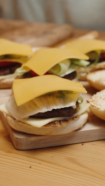 Vertical video. A Woman Places Slices of Cheese on the Burgers. Homemade Food. Ingredients Are Spread Out on the Table.