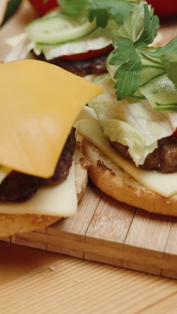 Vertical video. The Preparation of Burgers in a Homey Setting, slices of cheese are placed on top. Ingredients are on the table, and the burgers are almost ready. In slow motion.
