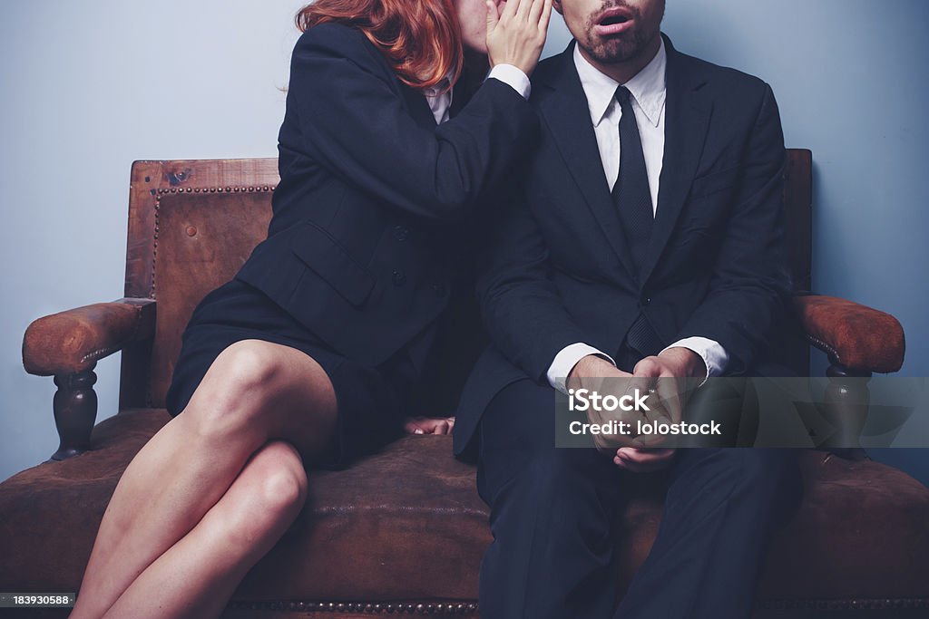 Gossip in the office lobby Young woman is gossiping to her male coworker who looks pretty astonished Gossip Stock Photo