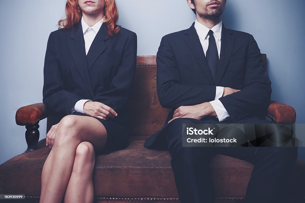 Man and woman waiting on a sofa Two sharply dressed business people are waiting on a sofa with a serious expression on their faces. Maybe they're waiting to enter a job interview, or maybe they're a couple waitng to see a divorce lawyer Gender Stereotypes Stock Photo