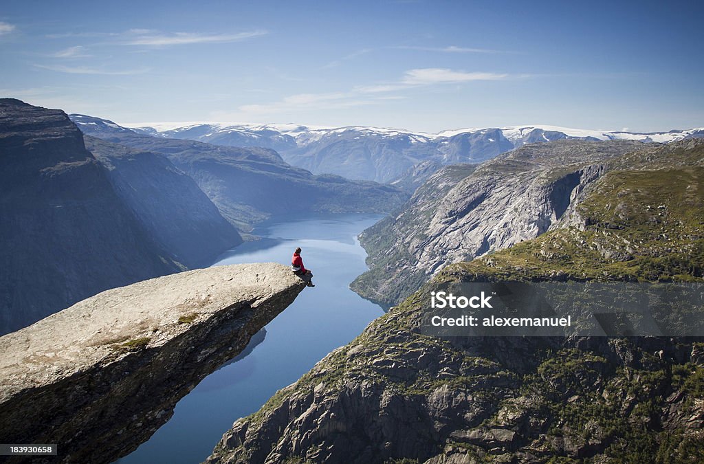 man sitting on trolltunga in norway man sitting on trolltunga rock above a norwegian fjord. Norway Stock Photo