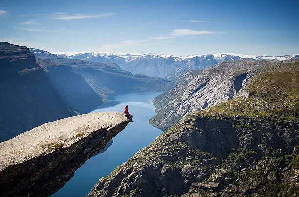 man sitting on trolltunga rock above a norwegian fjord.