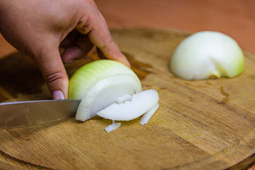 Woman cutting white onion on cutting board