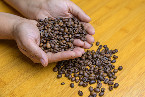 Hands holding roasted coffee beans on table