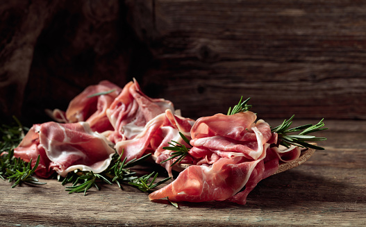 Italian prosciutto crudo or Spanish jamon with rosemary on an old wooden background. Copy space.