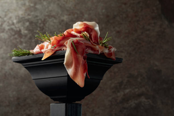 Prosciutto with rosemary on a black podium.