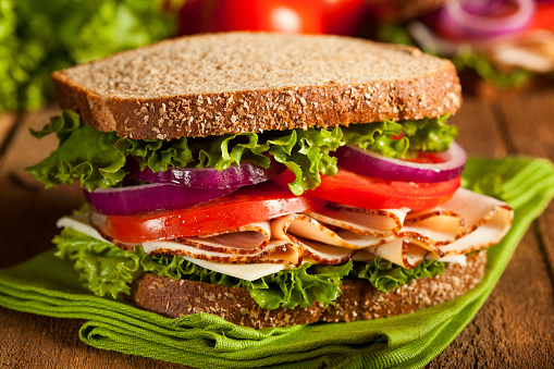 Side and front view of basic turkey sandwich with lettuce on brown bread in plastic baggie. White background.