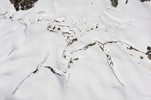 arial view of snow glide crack in mountains showing danger of avalanches in alpine landscape