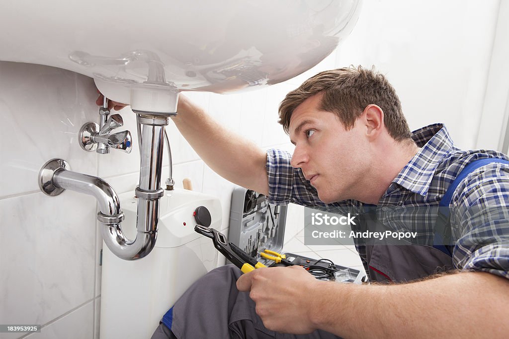 Young plumber fixing a sink in bathroom Portrait of male plumber fixing a sink in bathroom Plumber Stock Photo