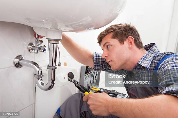 Young Plumber Fixing A Sink In Bathroom Stock Photo - Download Image Now - Plumber, Custodian, Repairing