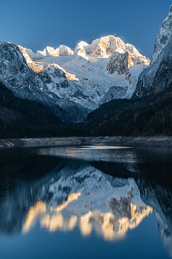 idyllic, calm, cold, late autumn mood at mountain lake in Austria, called Gosausee, with reflections in the water and spectacular snow covered Dachstein mounatin with glacier, blue sky, some wind at mountain peak