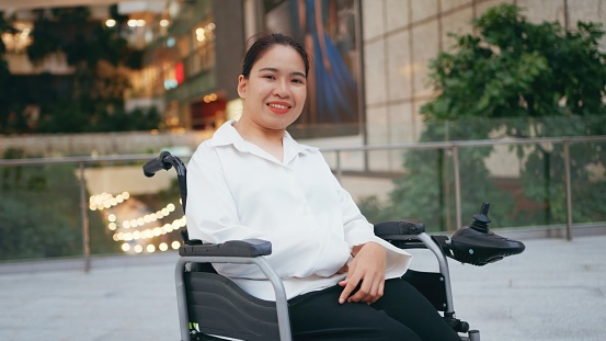Portrait of Smiling Asian disability freelance woman on wheelchair looking at camera. workforce hybrid workplace Remote Working.