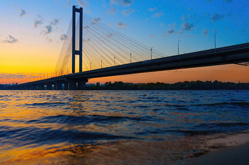 Sunset view of a cable-stayed bridge spanning across the Dnieper river seen from below.