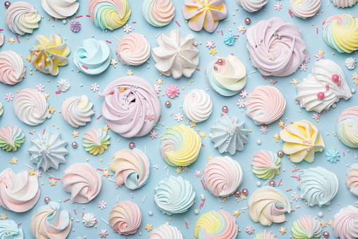 Top view of various shape multi colored meringue cookies and small sugar items on blue background