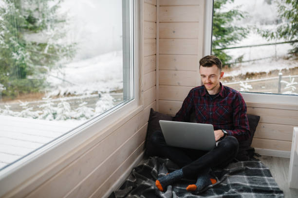 istock Remote work from cozy place. Man working on laptop in front of panoramic window with great view of mountains. Workplace in house in snowy morning. Wide interior view. Concept freelance lifestyle. 1839576813