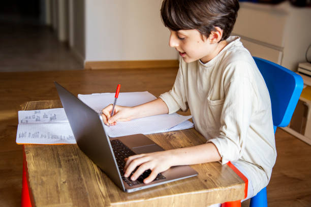 istock cheerful boy doing his homework at home using a laptop and writing in a notebook 1839582609