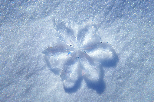 Top-down view of a large crystal snowflake ornament placed on fresh snow. Winter and holidays season related background.