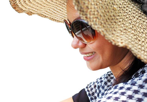 Young woman in a hat and sunglasses seating down on a white background and smiling