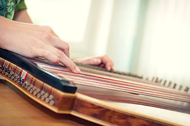 Close up of a young girl's hand playing on zither - musical instrument with strings.