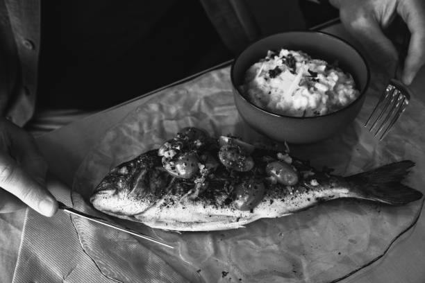 homme mangeant du poisson de daurade grillé et un risotto de légumes. photo noir blanc. - gourmet salad dinner prepared fish photos et images de collection