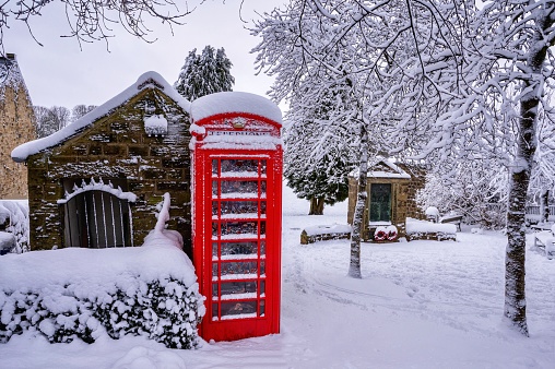 Idyllic snow covered red telephone Box /booth and war memorial in English countryside village