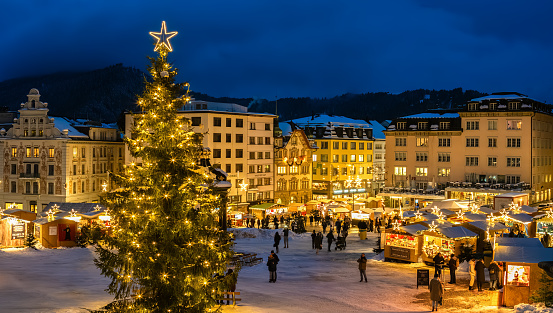 Einsiedeln, Switzerland - December 5, 2023: Christmas market and a big Cristmas tree in front of the Benedictine Abbey of Einsiedeln in blue hour