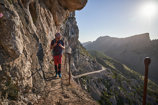 Full body of male traveler in activewear walking along narrow path near rock edge while enjoying amazing landscape in mountainous terrain