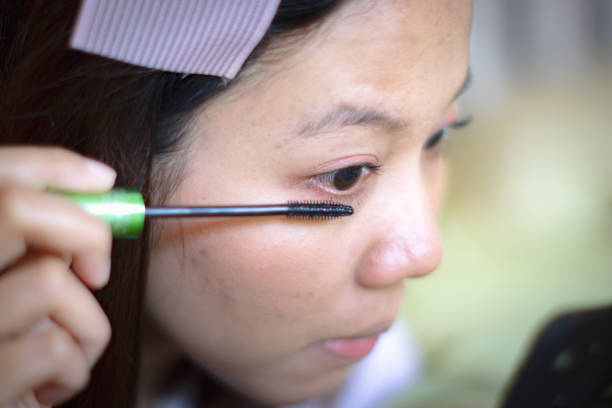 istock Pretty Asain woman applying make up (brush andpaint her eyelashes) in front of a mirror. Selective focus. 1839665806