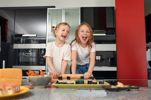 Two little girls siblings having fun and eating on the kitchen at home with japanese food.
