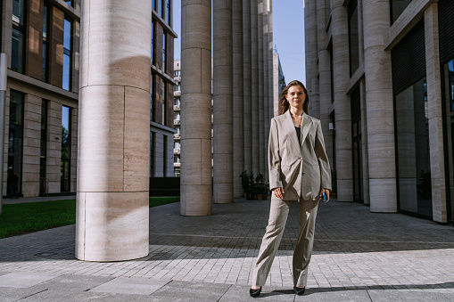 Purposeful brunette female lawyer standing at building with huge columns looks at camera feels confidence ready for any situations, independent women.