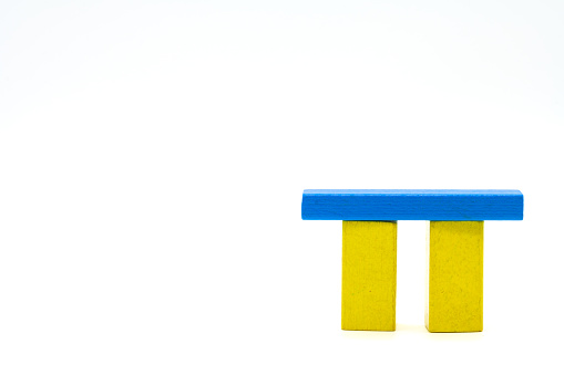 Two yellow wooden blocks standing isolated on a white background with a blue crossbar as a roof