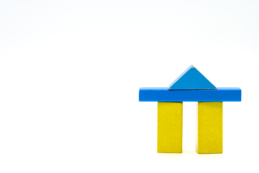 Two yellow wooden blocks standing isolated on a white background with a blue crossbar and triangle as a roof