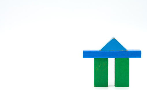Two green wooden blocks standing isolated on a white background with a blue crossbar and triangle as a roof