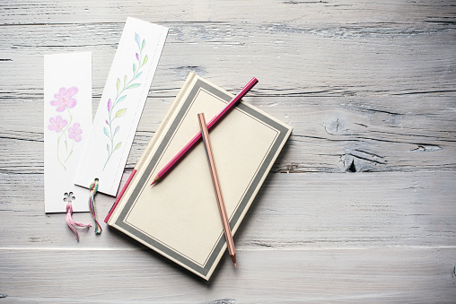 Flat Lay Concept of Notebook with Blooming Bookmarks on White Wooden Background