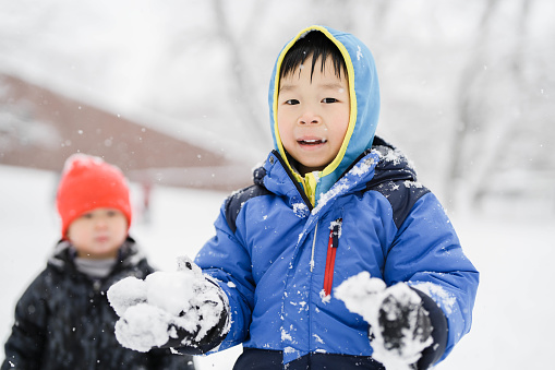 Cute little boy having fun and playing outdoors during snowfall