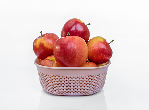 Red ripe Gala apples in a pink basket isolated on white background with reflection