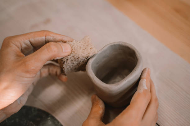 Female hands working with clay makes ceramic tableware on pottery workshop. Closeup of female hands working with clay makes tableware using hands tools on ceramic workshop. Woman creating ceramic product on pottery workshop. Process of creating minimalist handmade dinnerware. homemade pottery wheel stock pictures, royalty-free photos & images