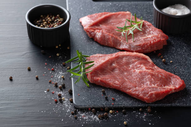 Two fresh raw marbled beef steaks on a cutting board on a wooden background with salt, pepper and rosemary in a rustic style