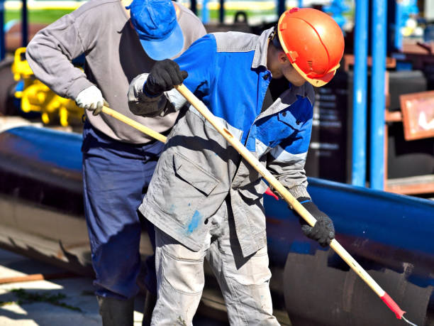 istock Two workers paint metal pipe black with paint rollers. Pipe treatment for corrosion protection. Metal paint. 1839778103