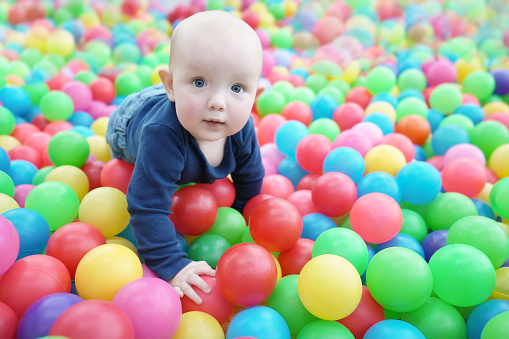 A cute eared baby crawls among bright multi-colored balls. Cute baby in the children's room. Close-up portrait