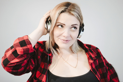 Young blonde woman in headphones on a white background. Close-up portrait. A beautiful girl listens to music and smiles, looking to the left.